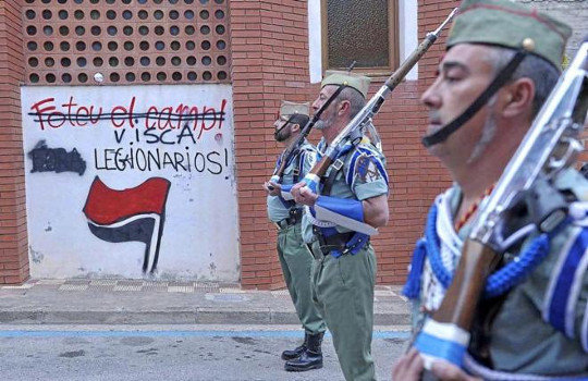 Legión desfilando en Palafolls ante un mural pintado por elementos de extrema izquierda